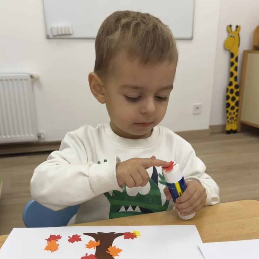 Хлопчик клеїть аплікацію осіннього дерева з паперовим листям